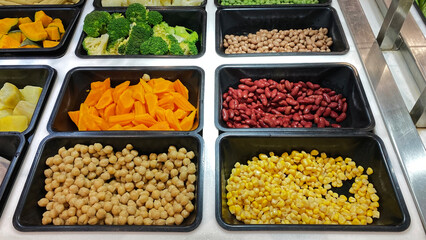 Colorful Salad Bar with Fresh Vegetables and Beans. A vibrant salad bar featuring fresh corn, chickpeas, red kidney beans, carrots, broccoli, and other vegetables. Ideal for promoting healthy eating,