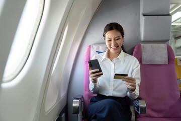 Payment Processing. Woman using smartphone and credit card on airplane.