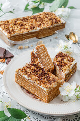 Homemade honey cake with sour cream and nuts on light background with cup of tea and spring flowers. Sweets, dessert and pastry, top view