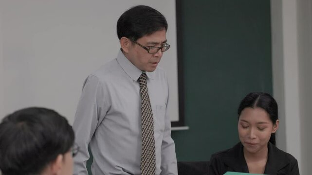 Lazy business team : Asian senior man supervisor gave the file to the team member who was using his mobile phone and was slacking off