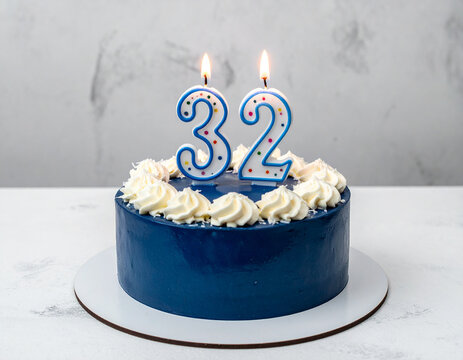 Beautiful cake with deep blue glaze with burning candle in shape of number 32. Tasty holiday dessert