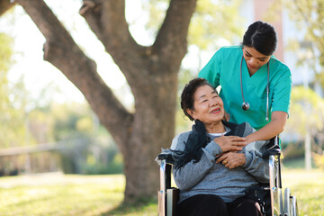 Nurse Taking Care of Elderly Asian Woman in Wheelchair ,Outdoor Healthcare Support.
