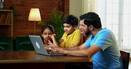 Family using laptop together at home sitting at dining table in modern living room, Indian parents children scrolling, surfing, planning vacation or shopping online while enjoying quality time