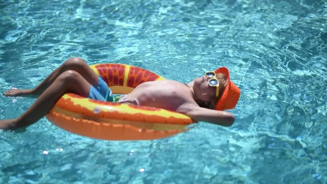 Swimming pool fun with happy kid. Kid splash in pool on summer day. Child rest on inflatable ring in swimming pool. Kid in poolside with floating toy. child with float ring in blue pool. Kids summer