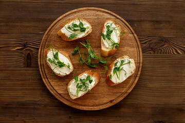 Toasts with fresh sprouting microgreens and cream cheese on wooden board, top view