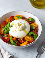 Bowl of burrata salad with cherry tomatoes, fresh basil leaves and drizzle of olive oil. Tasty food