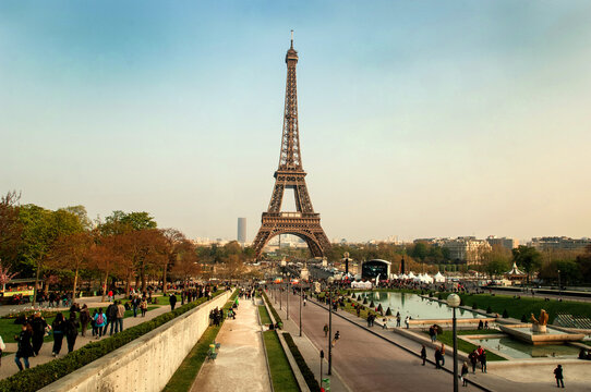 Horizontal view of the Eiffel Tower in Paris, France, captured head-on with the lush lawns of the Champ de Mars in the foreground. The iconic iron structure stands tall under a clear blue sky, framed 