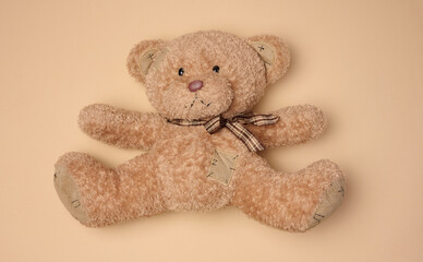 Fluffy brown teddy bear with a ribbon lying on a neutral background