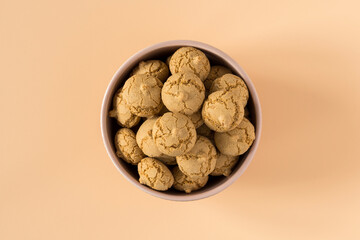 Amaretti cookie in a porcelain bowl on a beige background , top view , high-resolution . Delicious , crunchy biscuits for tea , flat lay .