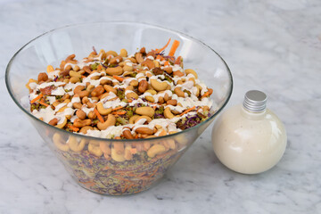 Fresh Broccoli Salad with Cashews in a clear glass bowl with broccoli florets, crunchy cashews, carrots, and red cabbage, drizzled with creamy white sauce bottle closeup side view of healthy salad