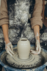 Close-up of artisan hands shaping clay vase on pottery wheel in studio with visible texture and...