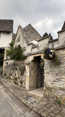 Historic stone wall with archway adorned by flowers on a quiet street in a charming village