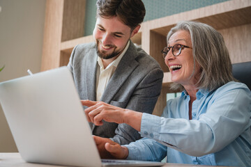 Obraz premium Two happy executive managers working on laptop discussing financial documents at meeting. Smiling friendly man and woman business professionals team talking planning project at work. Candid photo.