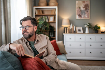 Pensive mature man pausing reading and looking out the window