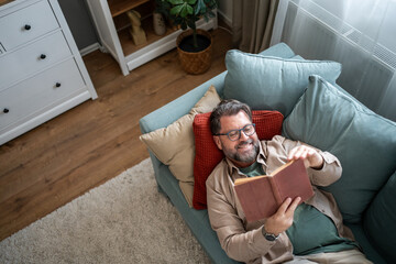 Smiling senior man reading a book on the sofa at home