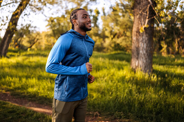 Young man jogging in a park during early morning surrounded by greenery and sunlight