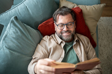 Fototapeta premium Happy senior man relaxing on sofa reading a book at home