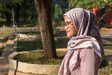 An Asian Muslim woman wearing a hijab and glasses poses outside