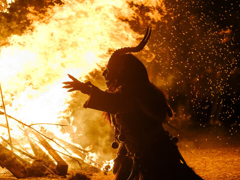 Silhouette of Krampus in a fur costume with horns, standing before a large bonfire. Krampus and St Nicholas, 5 December in mining village of Cave del Predil, Tarvisio, Italy.