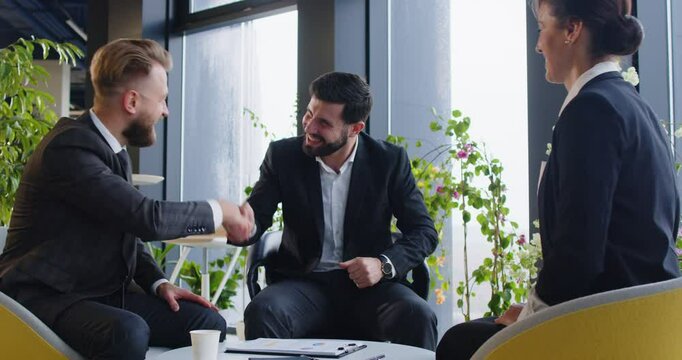 Group of people establishing good business relations and work partnership. Three happy smiling business partners meet in a modern office, make an agreement, exchange handshakes, and applaud each other