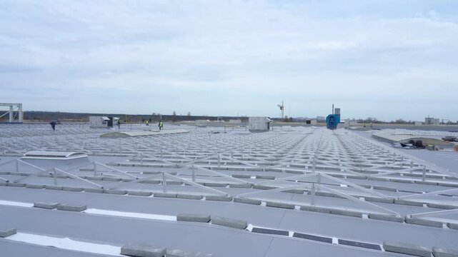 Workers install a frame and trusses to attach solar panels to the roof of a building.