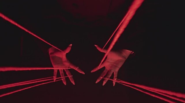 Hands Manipulating Red Strings in Dark Setting