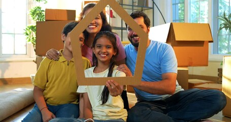 Looking through home shape cutout, Indian family holding paper house model and smiling with joy while shifting to new home, celebrating togetherness, ownership, and new beginnings in modern apartment