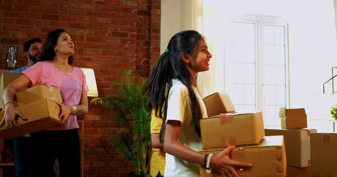 Family moving in new home holding cardboard boxes, Indian Asian young father, mother two kids enter lavish house surprised and happy, expressing joy and togetherness after shifting to new residence