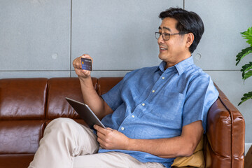 Asian senior man using tablet for online shopping with credit card at home