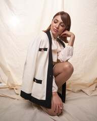 A fashionable woman wearing a chic white and black cardigan with a blouse and skirt, posing against...