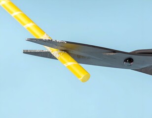 Yellow striped straw being cut by scissors on a light blue background. Minimalist concept.