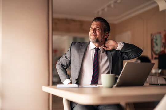 Businessman Stretching Neck While Working On Laptop Desk