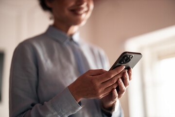 Woman Smiling While Using Smartphone Inside a Bright Room