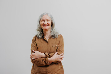 Smiling elderly woman with gray hair standing against a plain background in a casual outfit and relaxed pose during daylight