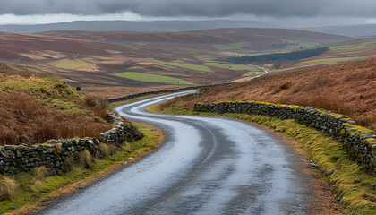 A winding rural road meanders through a hilly countryside with brown fields under an overcast sky, framed by stone walls