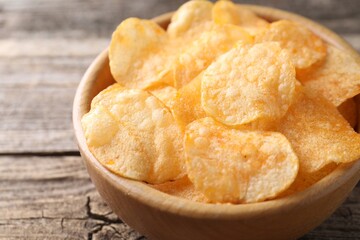 Tasty potato chips in bowl on wooden table, closeup