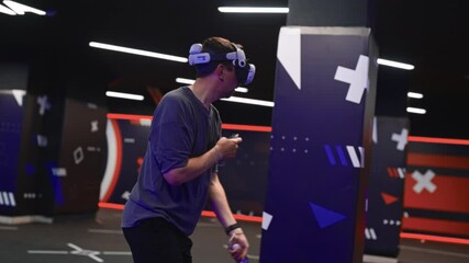 Man playing competitive VR shooter with friends at virtual reality lounge. Equipped with professional headset and motion controllers for immersive gameplay.