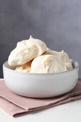 Delicious homemade meringue cookies in bowl on light table against gray background, closeup