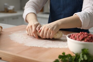 Making khinkali. Woman kneading dough at table in kitchen, closeup