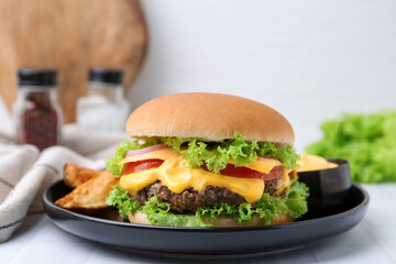 Tasty cheeseburger with sauce and potato wedges on white table, closeup