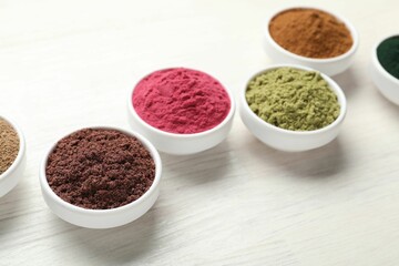 Different superfood powders on white wooden table, closeup