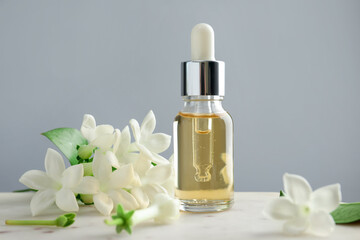 Bottle of essential oil and jasmine flowers on table against grey background, closeup