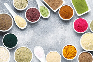 Frame of different superfood powders on grey textured table, flat lay. Space for text