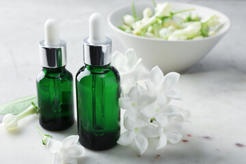 Bottles of essential oils and jasmine flowers on table, closeup