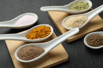 Different superfood powders in spoons on dark textured table, closeup