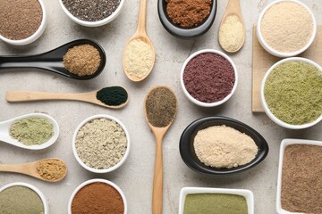 Different superfood powders in spoons and bowls on grey textured table, flat lay