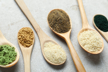 Different superfood powders in spoons on grey textured table, closeup