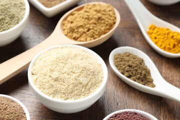 Different superfood powders in bowls and spoons on wooden table, closeup