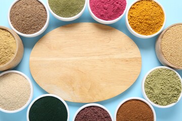 Different superfood powders in bowls and wooden board on light blue background, flat lay. Space for text