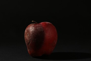 One rotten red apple on black background